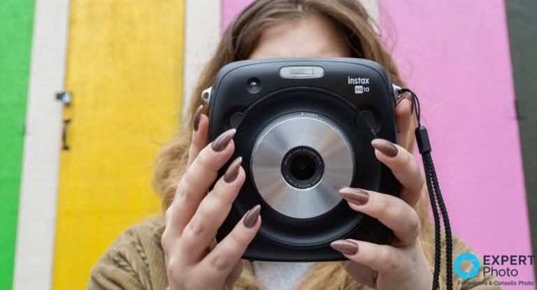 Test Instax Square SQ10 : l’hybride carré qui tient encore en occasion Fujifilm Instax Square SQ10 posé sur carrelage vert, vue plongeante, objectif argenté et fente d'éjection film visibles