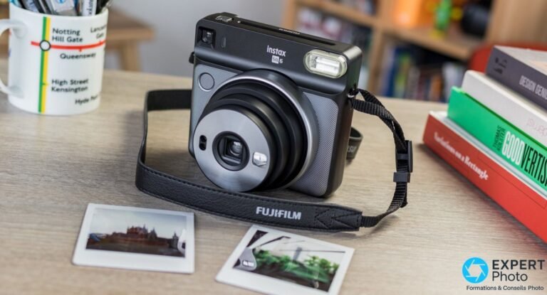 Test Fujifilm Instax Square SQ6 : avis terrain et achat en 2026 Boîtier Fujifilm Instax SQ6 noir et gris en vue trois quarts avant, bandoulière FUJIFILM, deux tirages carrés sur table