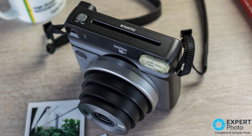 Fujifilm Instax SQ6 vu en plongée, objectif déployé, interrupteur OFF/ON et fente d'éjection des tirages visibles