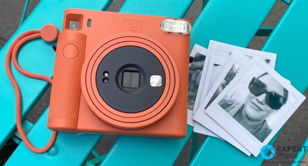 Instax Square SQ1 terracotta posé sur chaise turquoise, dragonne orange, quatre tirages square noir et blanc en éventail à côté
