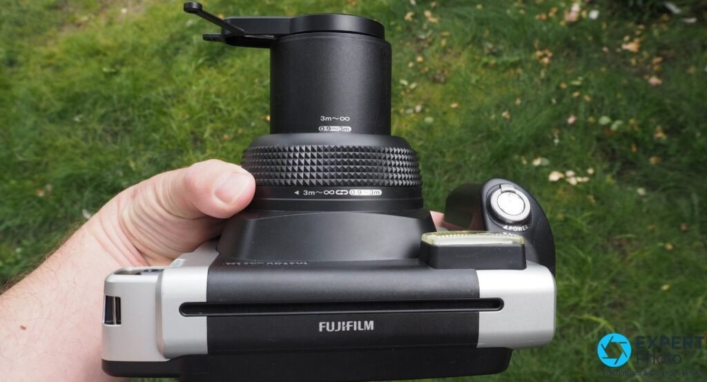  Fujifilm Instax Wide 300 en main, bonnette gros plan montée sur l'objectif, vue de dessus en extérieur sur gazon