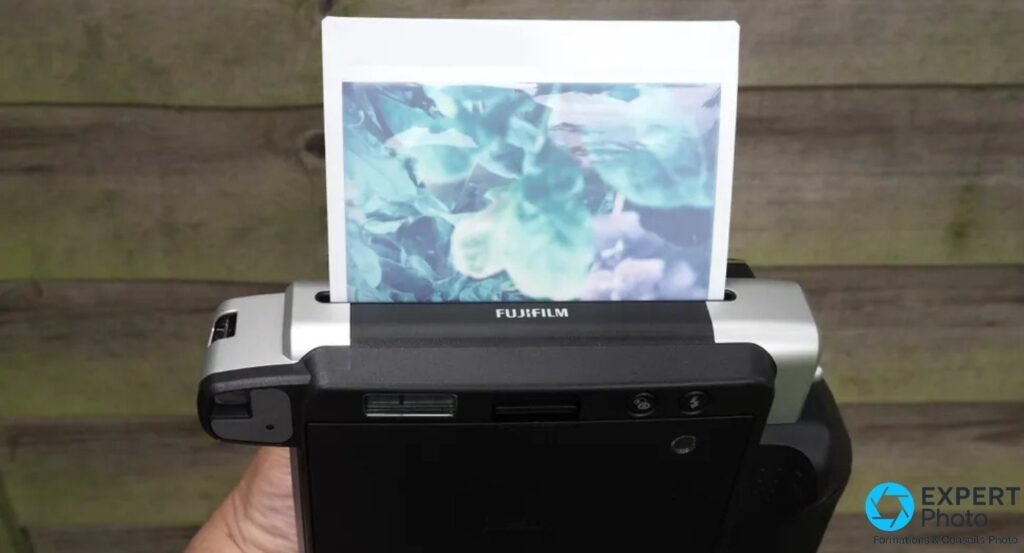 Fujifilm Instax Wide 300 tenu en main, vue arrière, tirage Wide couleur feuillage sortant de la fente d'éjection du boîtier