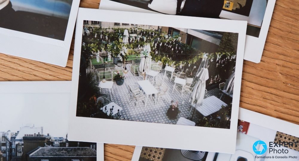 Tirages Instax Wide éparpillés sur une planche en bois, le central montre une terrasse fleurie vue de haut