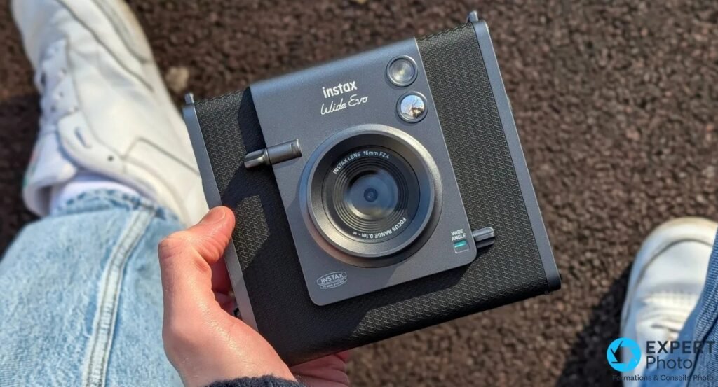 Instax Wide Evo noir tenu en main, face avant, objectif 16mm F2.4 et mention Wide Angle visibles
