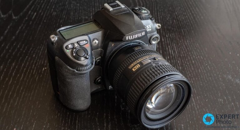 Fujifilm S5 Pro posé sur bois foncé, vue trois-quarts avant, zoom Nikon AF-S DX 16-85mm VR monté, marquage S5 Pro visible.