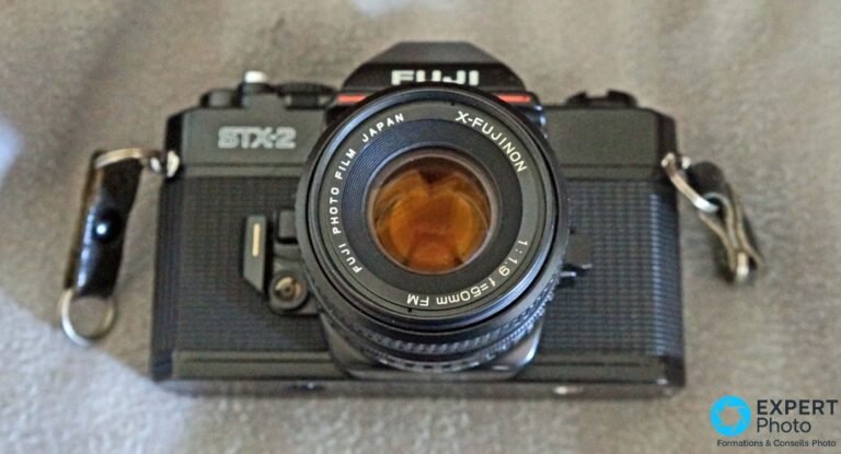 Fujifilm STX-2 noir vu de face, objectif X-Fujinon 50mm f/1.9 monté, diaphragme ouvert laissant apparaître le miroir orange.