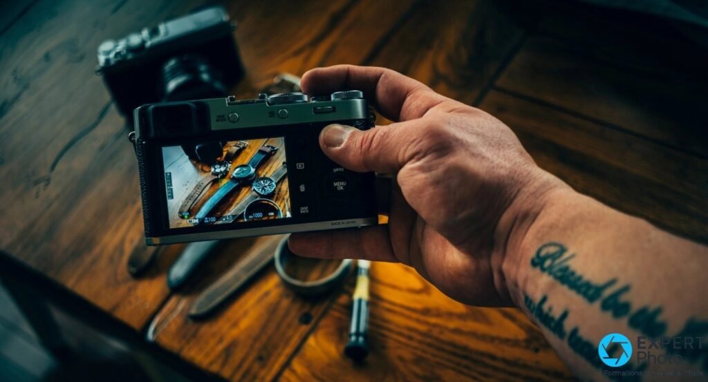 Fujifilm X100F en main, écran LCD arrière affichant une scène de montres avec réglages M, ISO 100, f/4, 1/1000 s visibles.