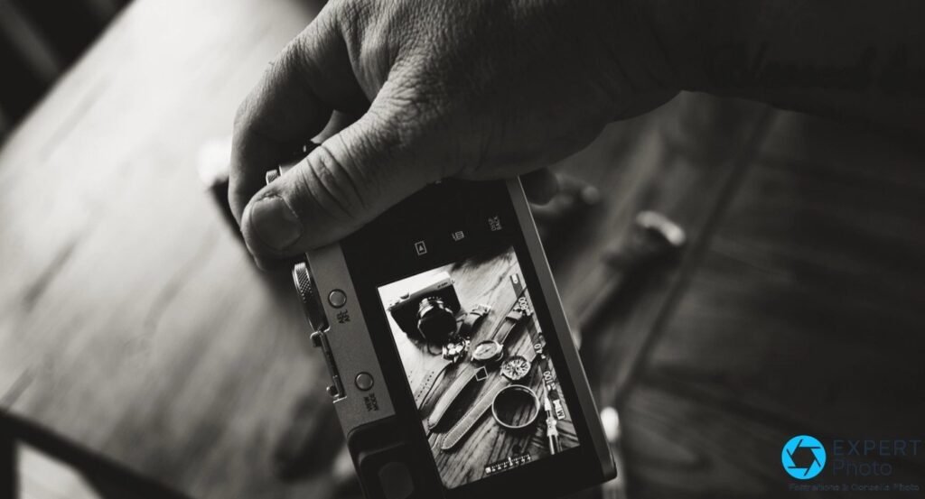 Fujifilm X100F argent tenu à la main, vue arrière montrant l'écran LCD avec une photo composée de montres et bracelets.
