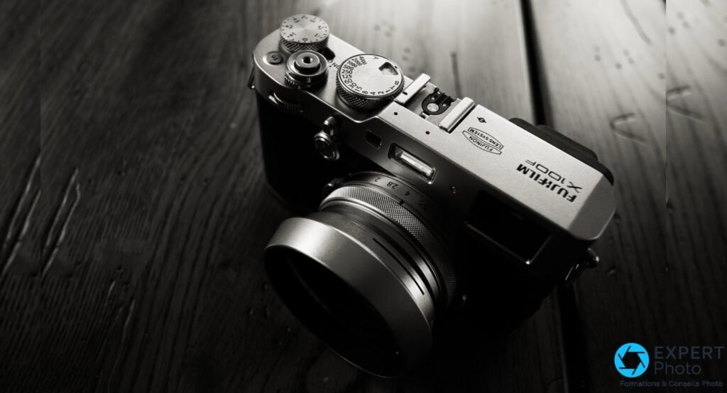 Fujifilm X100F argent vu de dessus, logo visible, molettes vitesse et ouverture, pare-soleil monté sur l'objectif.