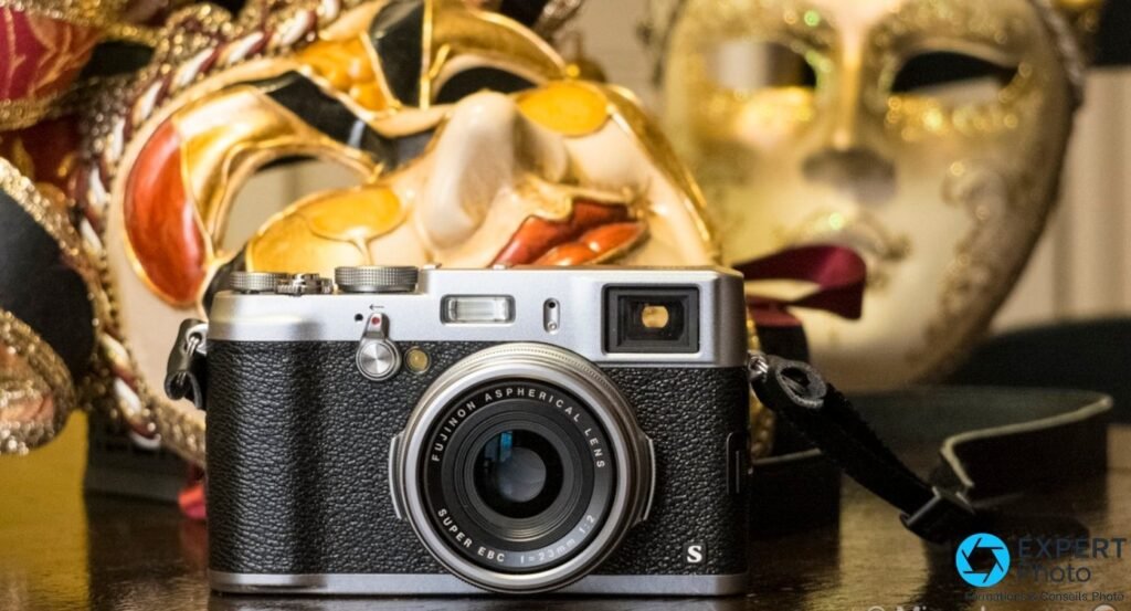 Fujifilm X100S vu de face, objectif Fujinon 23 mm f/2 centré, flash et viseur hybride visibles sur capot argenté.