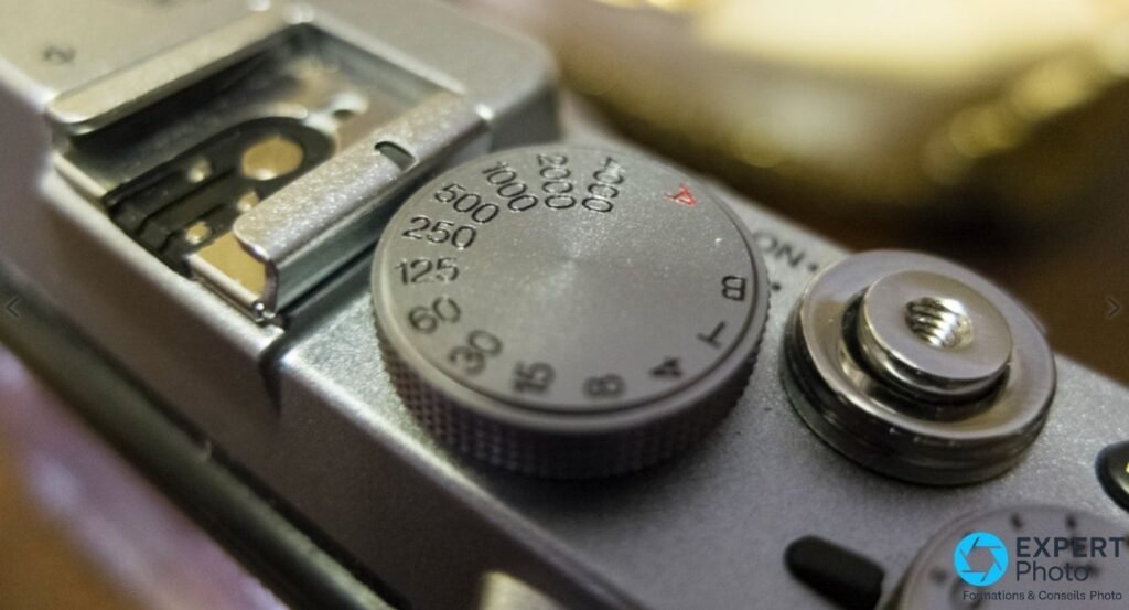 Dos du Fujifilm X100S : écran LCD allumé affichant mode M 1/500 F5.6 ISO 200, viseur, joystick MENU et touches AE/DRIVE. 