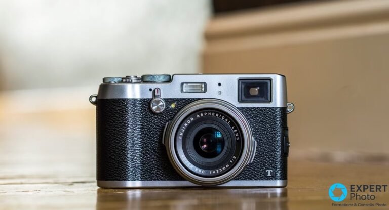 Fujifilm X100T posé sur un plan en bois, face avant, objectif fixe Fujinon 23mm f/2 et viseur hybride visibles.