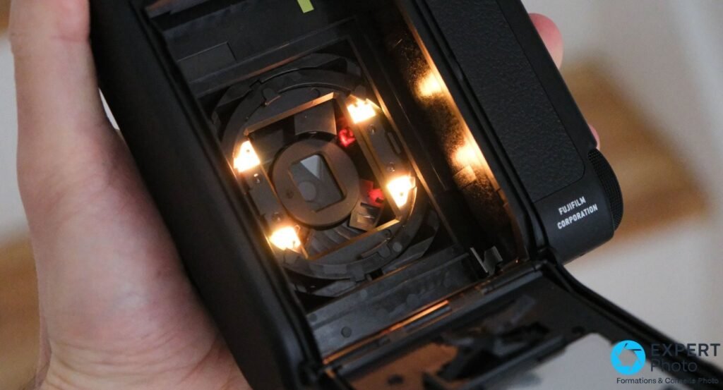 Instax Mini 99 compartiment film ouvert, mécanisme d'éjection éclairé, mention Fujifilm Corporation sur la coque