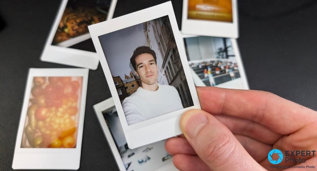 Main tenant un tirage Instax Mini portrait d'homme en pull blanc, fond urbain, autres tirages sur surface noire