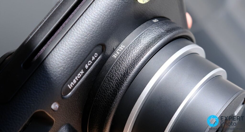 Gros plan sur la bague de mise au point Instax SQ40, inscriptions SELFIE et NO visibles, finition grain de cuir noire