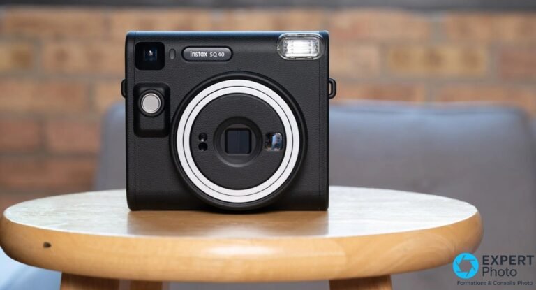 Fujifilm Instax Square SQ40 noir face avant, posé sur table ronde en bois, fond mur brique flou, flash et viseur visibles
