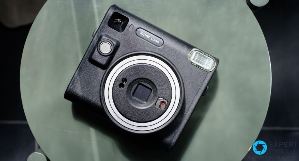 Fujifilm Instax Square SQ40 noir posé en biais sur table ronde verte, vue légèrement plongeante, logotype visible 
