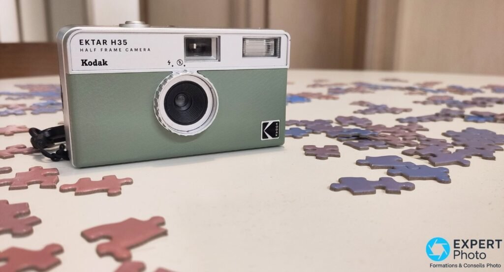 Dos du Kodak EKTAR H35 noir avec LED rouge Ready du flash, porte pile AAA et bandoulière noire posée à côté.