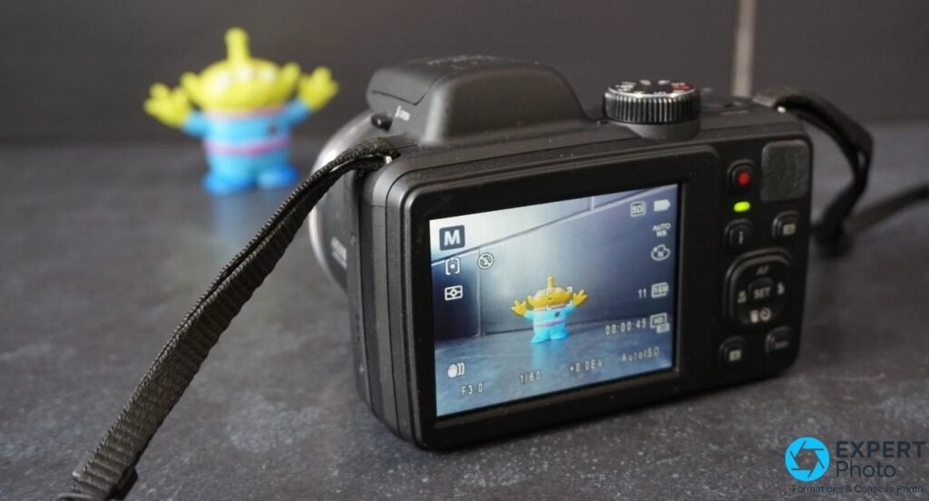 Kodak Pixpro AZ401 vu de dos, écran LCD allumé en mode M, réglages F3.0 1/60 AutoISO lisibles, figurine visible à l'écran