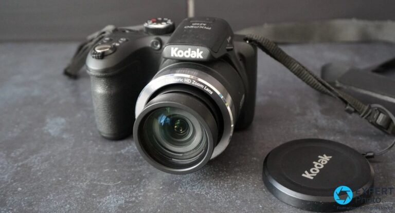 Kodak Pixpro AZ401 de face sur fond gris, objectif HD Zoom Lens centré, capuchon Kodak posé à droite, dragonne visible