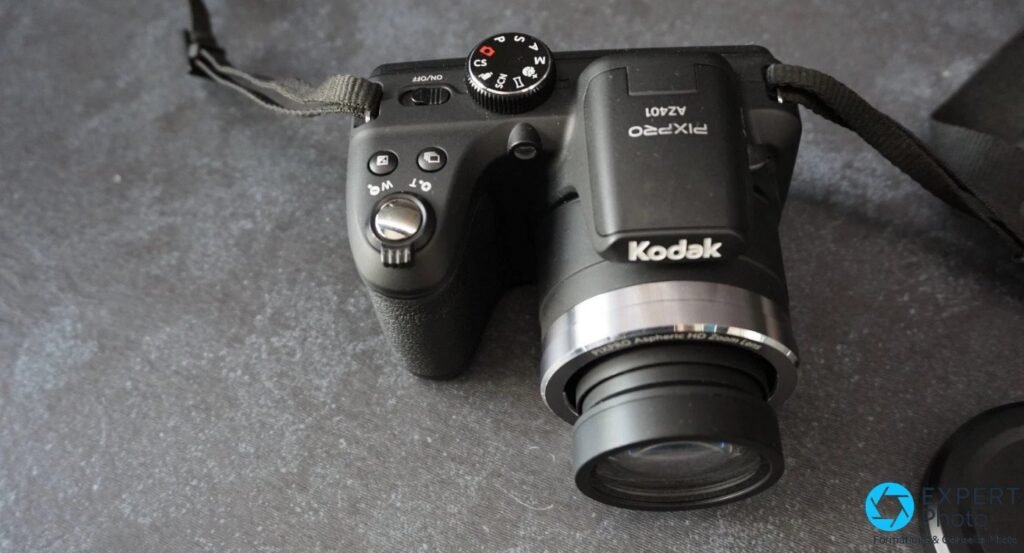 Kodak Pixpro AZ401 en vue trois quarts de dessus, molette modes visible, objectif zoom déployé, logo Kodak, sangle textile