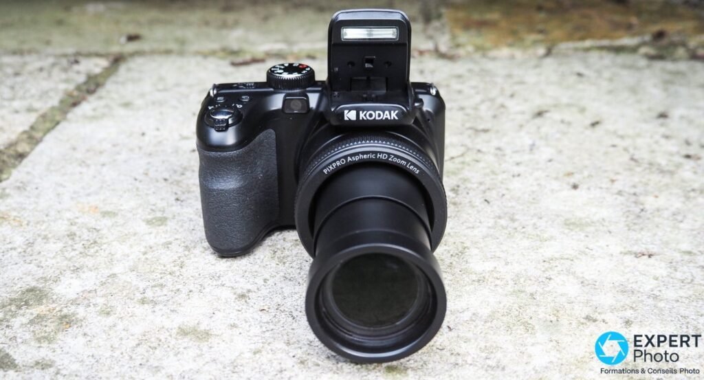 Kodak PIXPRO AZ425 tenu de dessus, zoom déployé, badge Full HD, SDXC, molette PSAM et boutons commande visibles