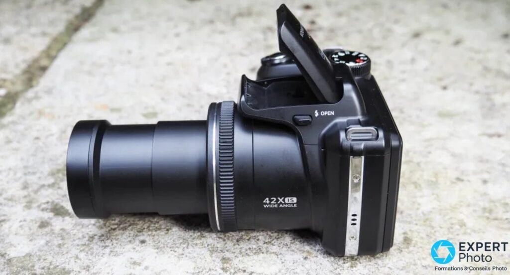 Kodak PIXPRO AZ425 sur sol pierre, face avant, objectif 42x entièrement sorti, flash pop-up relevé, fond pierre grise