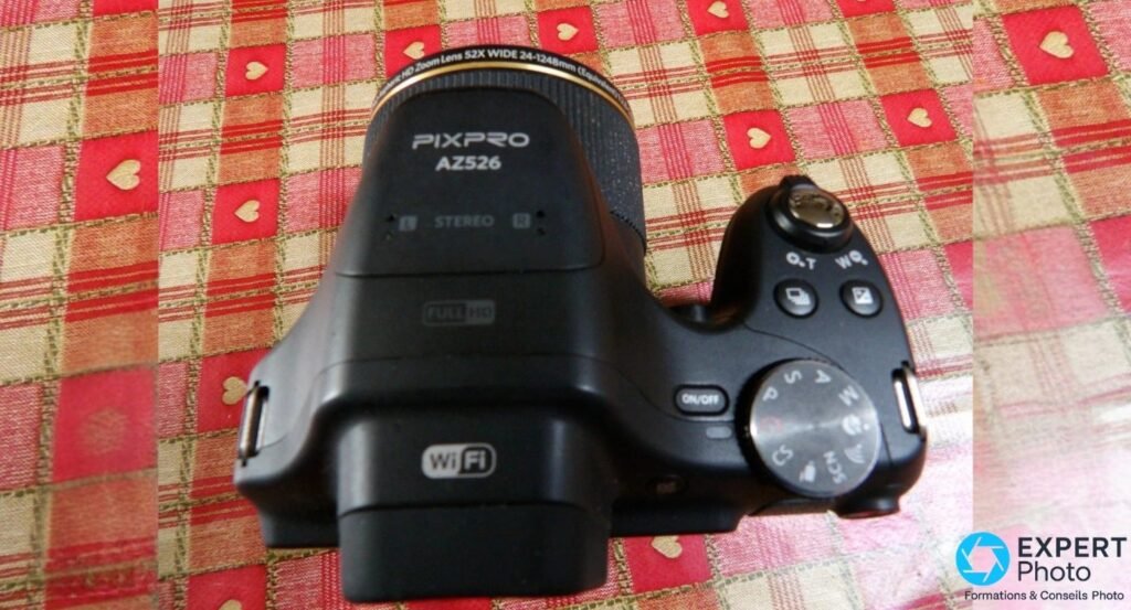 Kodak PIXPRO AZ526 vu de dessus, mentions PIXPRO AZ526, STEREO, FULL HD et Wi-Fi visibles, molette de modes PASM à droite.