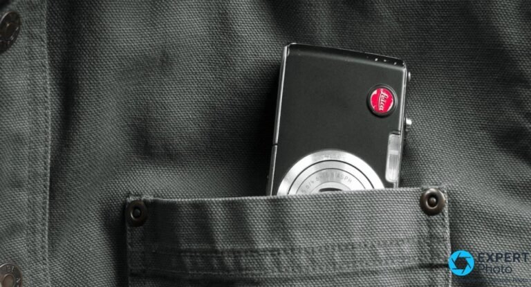 Leica C-Lux 1 vu de dessus dans une main, nom gravé, zoom optique sorti et déclencheur chromé apparents