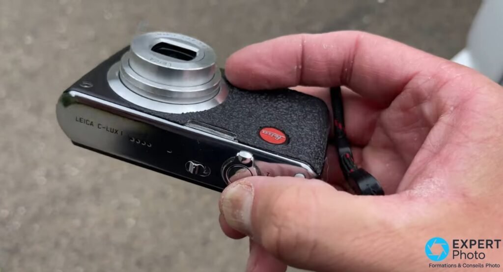 Dos noir du Leica C-Lux 1 avec logo rouge Leica, glissé dans la poche poitrine d'une chemise en toile grise