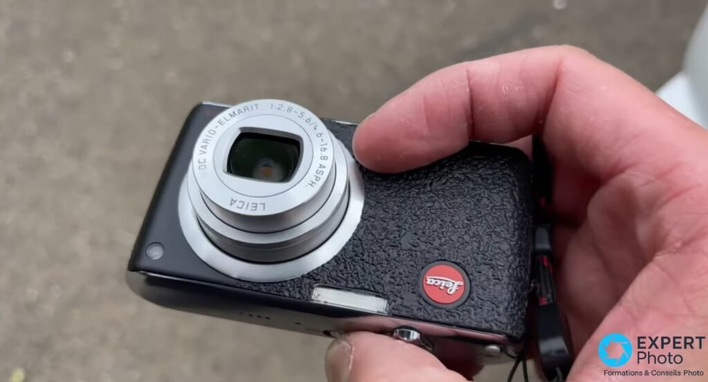 Face avant du Leica C-Lux 1, objectif Leica DC Vario-Elmarit 1:2.8-5.6 déployé, logo rouge sur la poignée noire