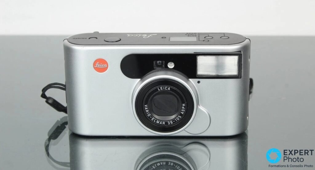 Leica C1 argentique vu de face sur fond gris, logo Leica rouge, flash, viseur et objectif Vario-Elmar visibles