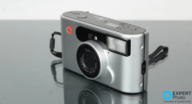 Leica C1 argentique trois quarts avant, objectif Vario-Elmar visible, dragonne noire et reflet sombre