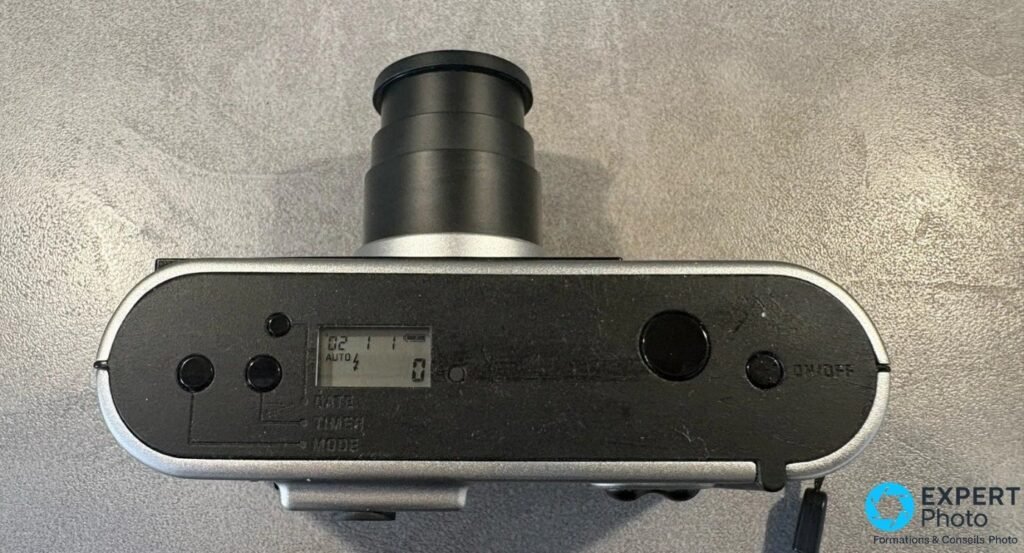 Leica C3 vu de dessus, zoom 28-80 mm sorti, écran LCD allumé, boutons mode date timer et déclencheur visibles