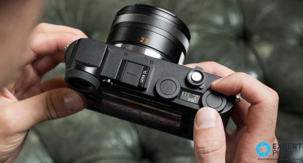 Leica CL vu du dessus, mains tenant le boîtier avec objectif Summicron-TL 23mm, deux molettes et écran d'état visibles 