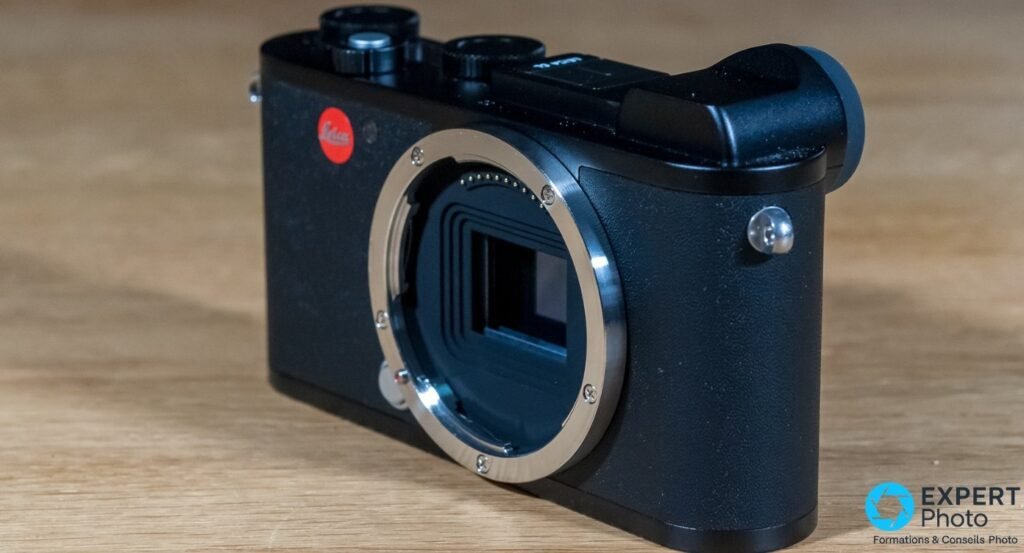 Leica CL boîtier nu vu de face trois-quarts sur table en bois, monture L et capteur APS-C visibles, logo Leica rouge