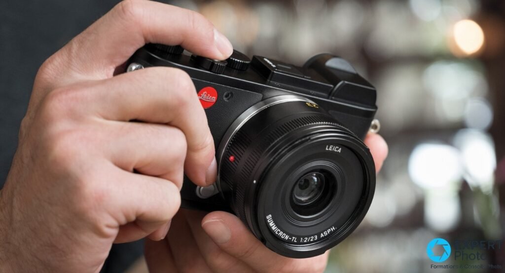 Leica CL avec Summicron-TL 23mm f/2 ASPH tenu en position de prise de vue, intérieur de commerce en arrière-plan flou