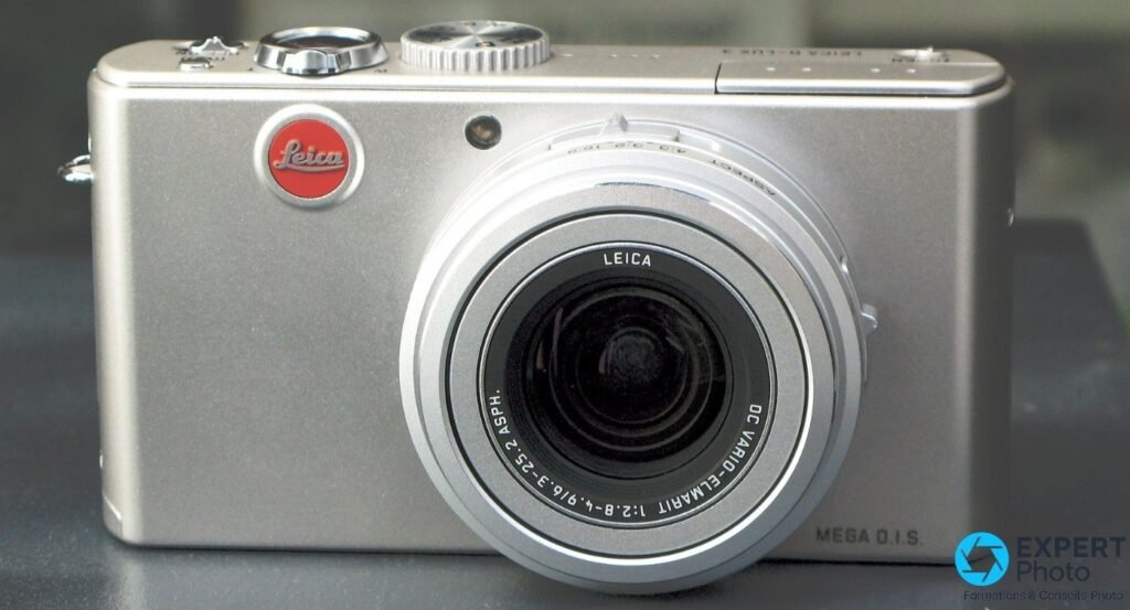 Compact Leica D-Lux 2 argent vu de face, objectif Leica DC Vario-Elmarit déployé en téléobjectif sur fond gris foncé