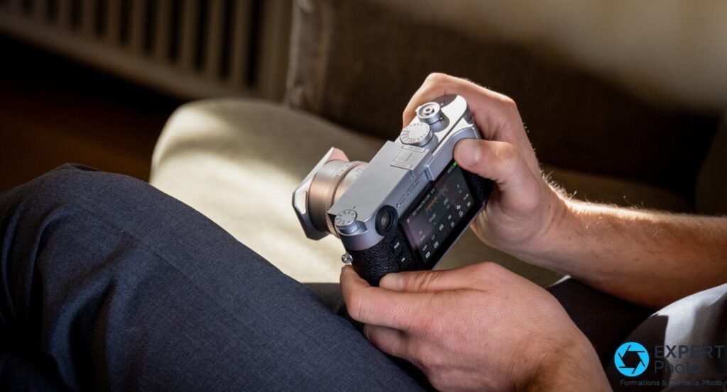  Leica M11 argenté tenu à plat sur les genoux d'un photographe, écran tactile affichant un menu de réglages. 
