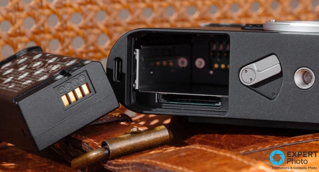 Leica M11 Monochrom : batterie sortie côté contacts, port USB-C et logement de carte SD visibles dans la base.