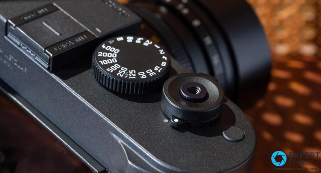 Leica M11 Monochrom : molette de vitesses graduée jusqu'à 1/4000 s et accessoire rond monté près de la griffe. 