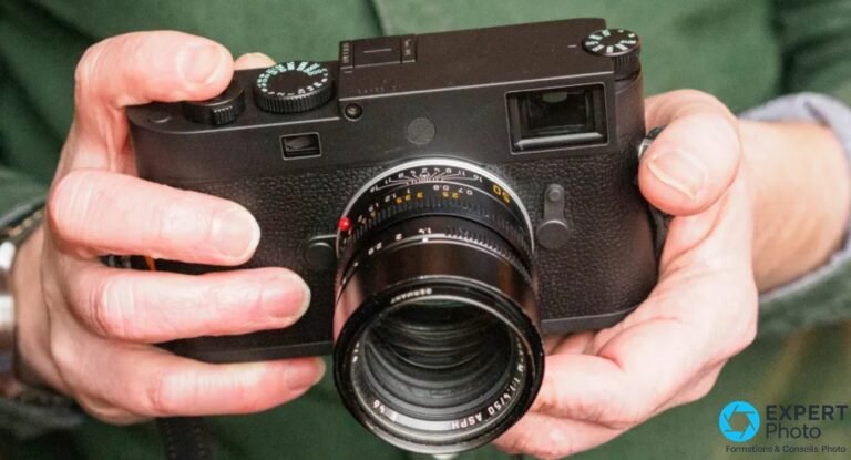Leica M11 Monochrom tenu à deux mains de face, équipé du Summilux-M 50 mm f/1,4 ASPH, sur fond de pull vert.