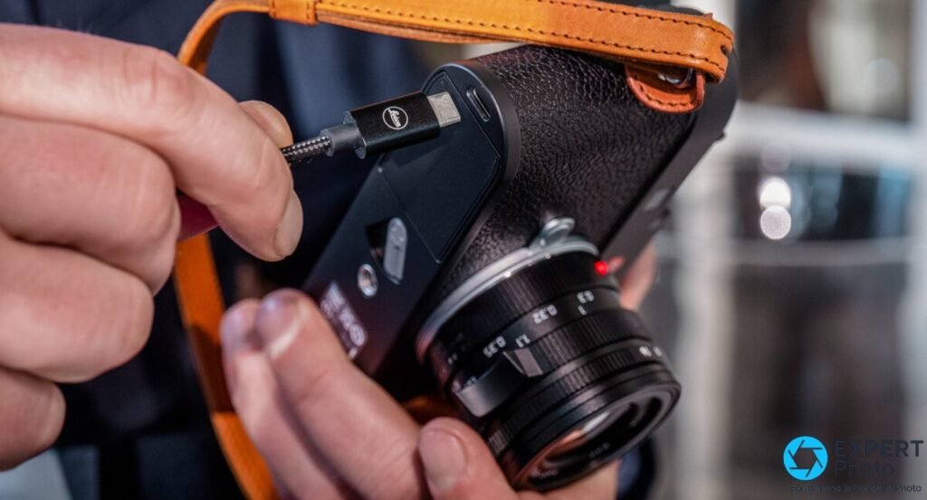 Câble USB-C gravé Leica en cours de branchement sur le port d'un Leica M11 logé dans un étui demi-cuir. (