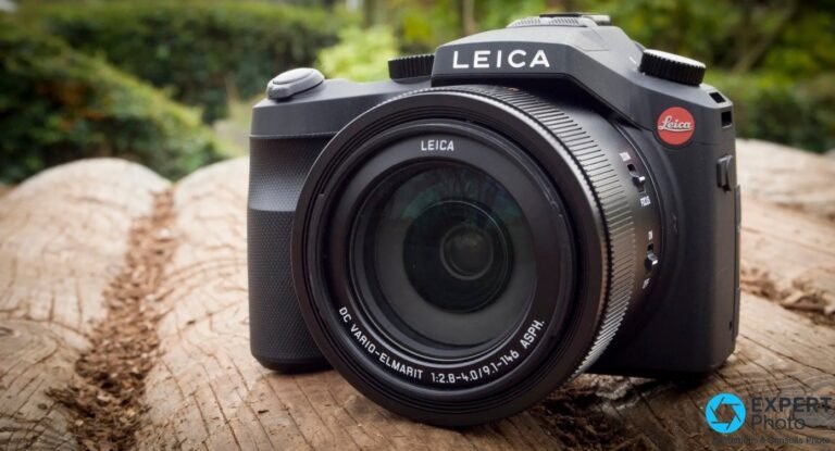 Leica V-Lux Typ 114 vu de face, objectif DC Vario-Elmarit 2.8-4.0 déployé, posé sur un tronc en jardin