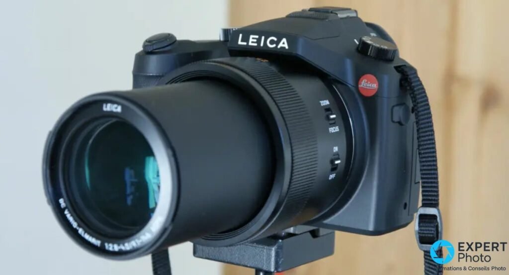 Leica V-Lux Typ 114 vu de profil avec le zoom 25-400 mm déployé, sélecteur zoom/focus visible, sangle noire 