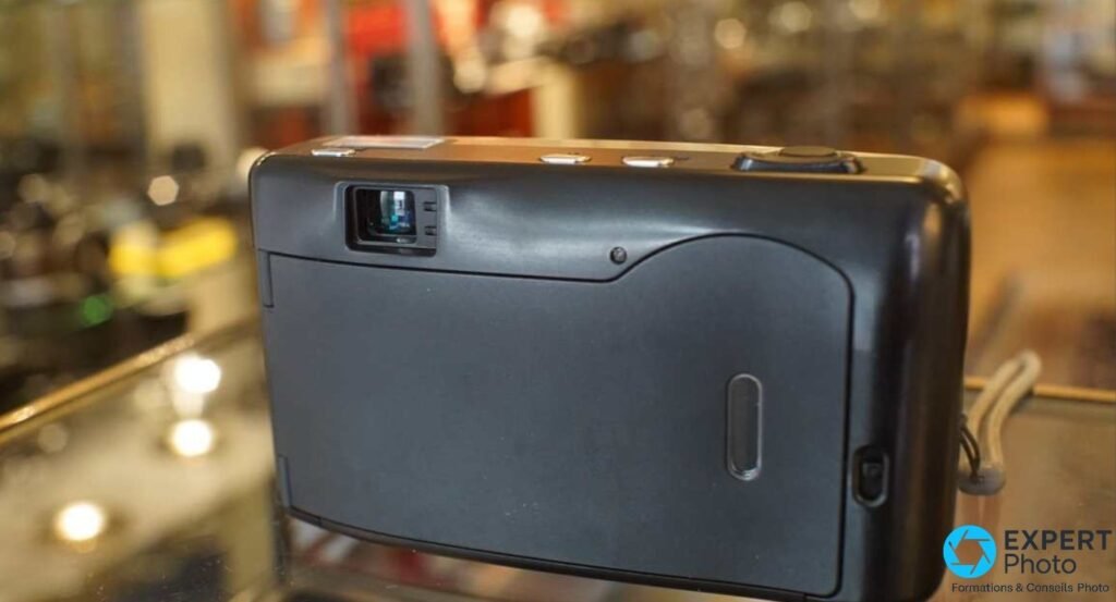  Leica Z2X vu de dos avec viseur optique, compartiment pellicule, dragonne grise, posé sur une vitrine de boutique