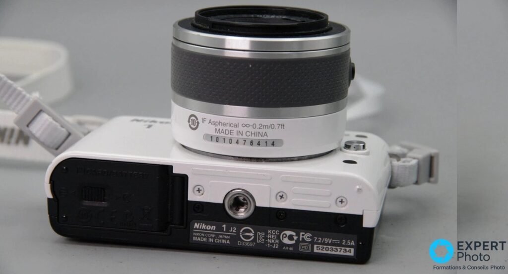 Dessous du Nikon 1 J2 blanc avec plaque Nikon 1 J2 Made in China, filetage trépied central et trappe carte/batterie fermée 