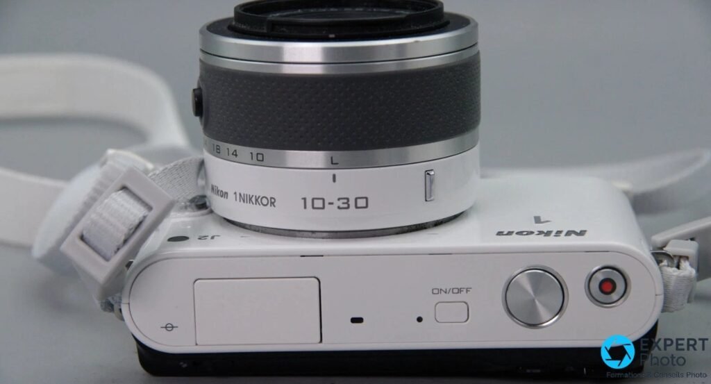 Dessus du Nikon 1 J2 blanc avec bouton ON/OFF, déclencheur, molette et bouton d'enregistrement vidéo rouge, objectif 10-30mm