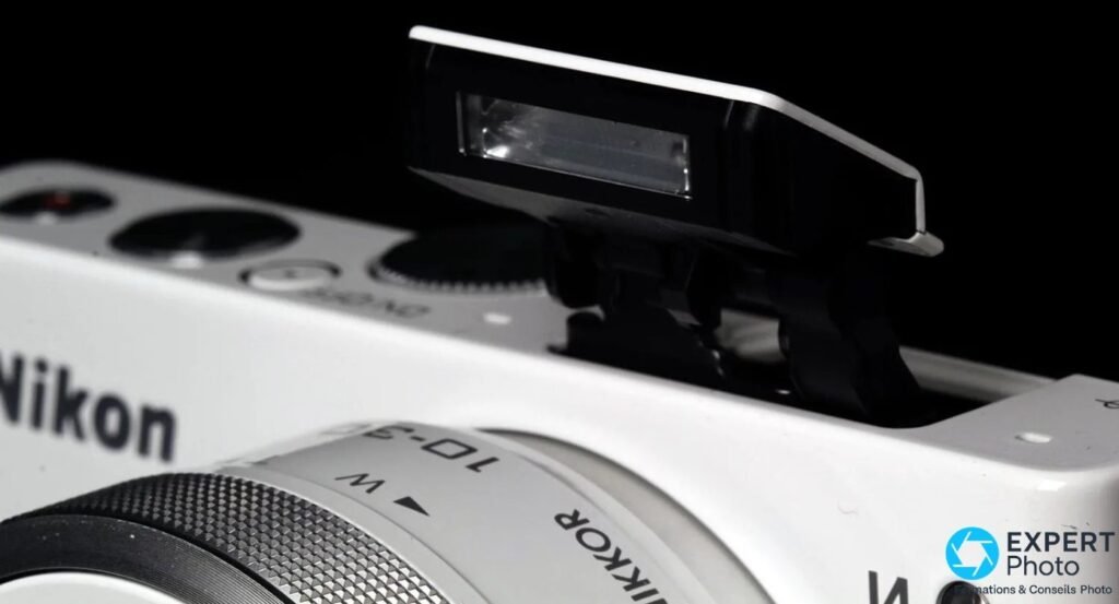 Flash pop-up intégré du Nikon 1 J4 relevé en position active, molettes de commande et objectif visibles au premier plan