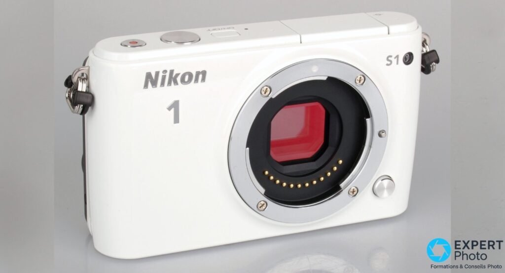 Boîtier Nikon 1 S1 blanc nu sans objectif, monture Nikon 1 CX visible, capteur apparent et contacts électroniques dorés. 